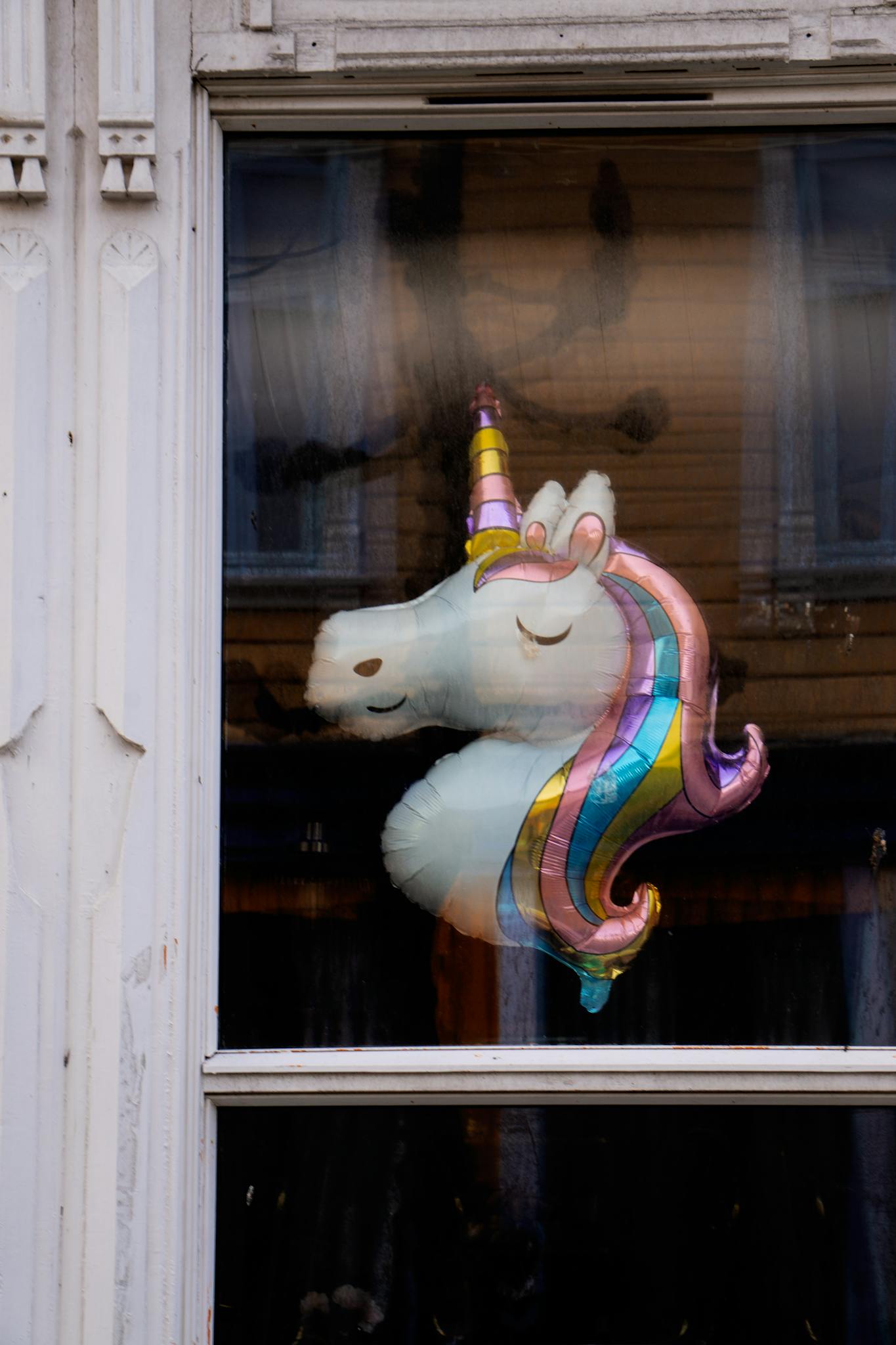 A vibrant unicorn balloon displayed in an urban window setting.